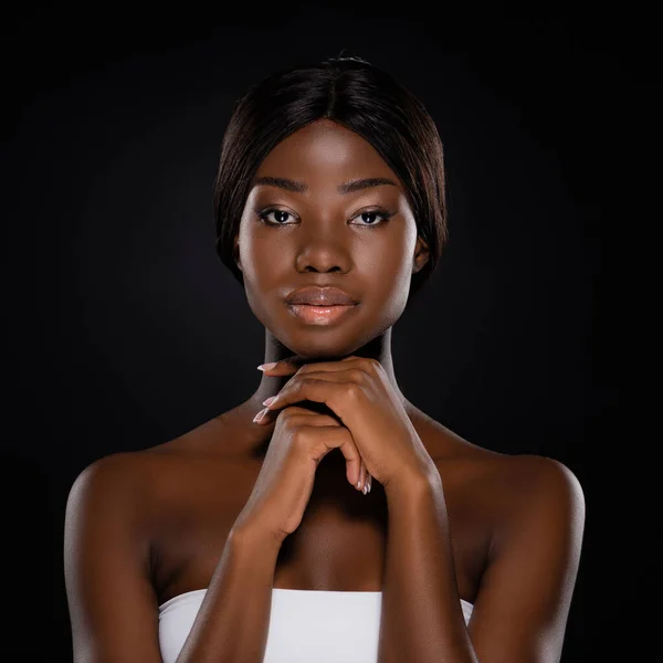 African american woman with hands under chin looking at camera isolated on black — Stock Photo