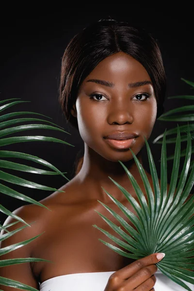 African american woman near green palm leaves isolated on black — Stock Photo