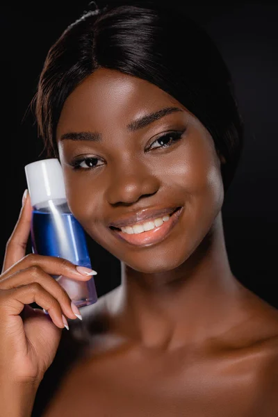 Portrait of african american naked woman holding micellar water isolated on black — Stock Photo
