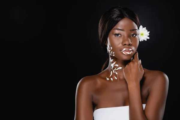 Mujer afroamericana con crisantemo blanco en pelo y pétalos en cuello y labios aislados en negro - foto de stock