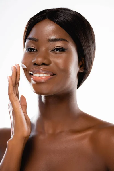 Mujer desnuda afroamericana aplicando crema cosmética en la cara aislada en blanco - foto de stock