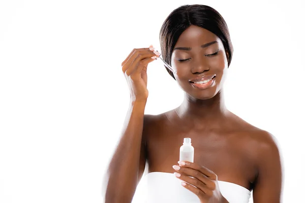 Mujer afroamericana con los ojos cerrados aplicando suero en la cara aislada en blanco - foto de stock