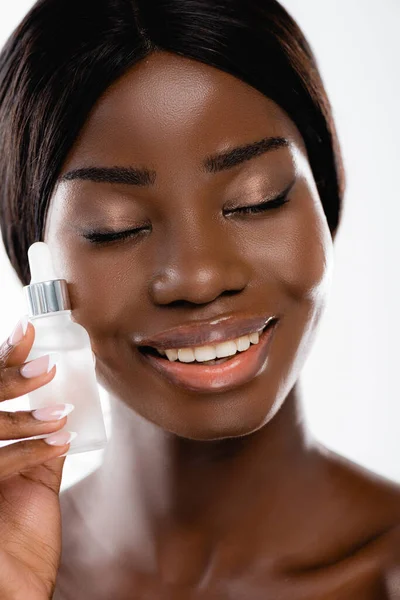 Femme américaine africaine nue avec les yeux fermés tenant bouteille de sérum isolé sur blanc — Photo de stock