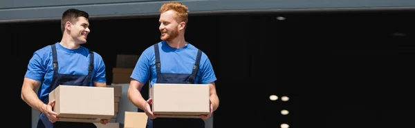Panoramic orientation of movers holding cardboard boxes and looking at each other on urban street — Stock Photo