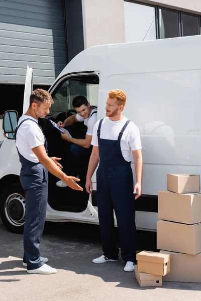 Lader schaut Kollege an und zeigt auf Pappkartons neben Lkw auf der Stadtstraße — Stockfoto