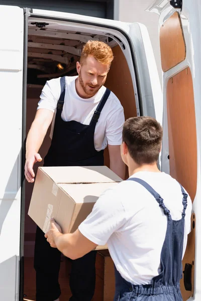 Selective focus of loader giving carton box to colleagues while unloading truck outdoors — Stock Photo