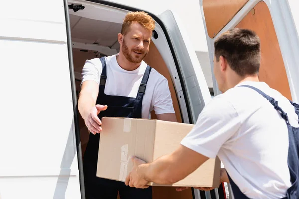 Selective focus of loader in overalls giving cardboard box to colleague in truck — Stock Photo