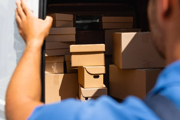 Cropped view of loader standing near cardboard boxes in truck outdoors — Stock Photo
