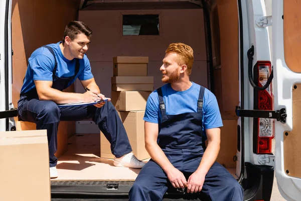 Selective focus of loader with pen and clipboard looking at colleague near cardboard boxes in truck — Stock Photo