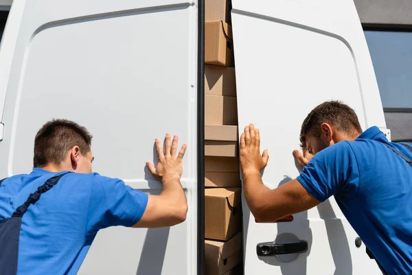 Back view of loaders closing doors of truck with cardboard boxes on urban street — Stock Photo