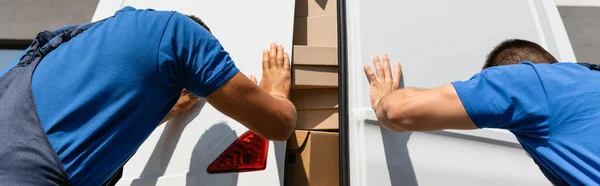 Horizontal crop of movers in uniform closing cardboard boxes in truck on urban street — Stock Photo