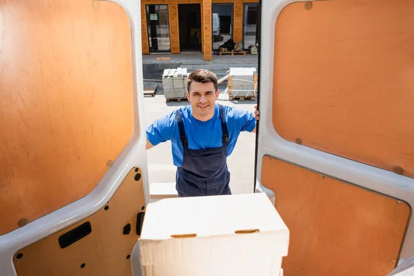 Selective focus of loader looking at camera near package in truck on urban street — Stock Photo