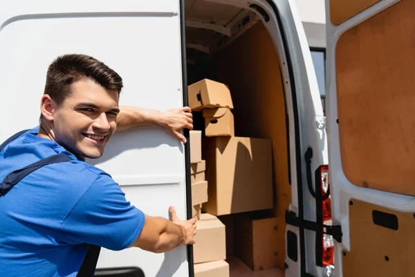 Chargeur regardant la caméra tout en fermant la porte du camion avec des paquets à l'extérieur — Photo de stock