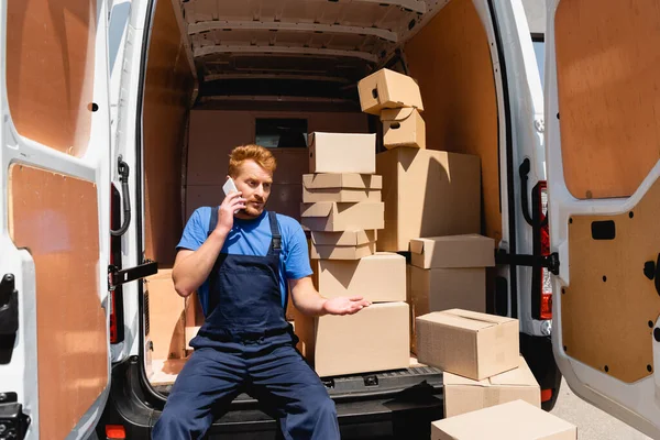 Lader spricht auf Smartphone, während er im Freien in der Nähe von Paketen im Lastwagen sitzt — Stockfoto