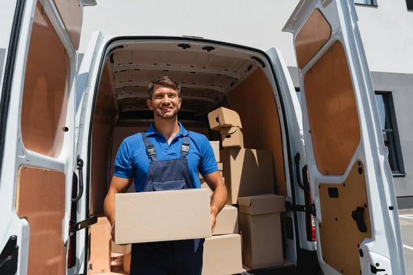 Loader in overalls holding package near truck on urban street — Stock Photo