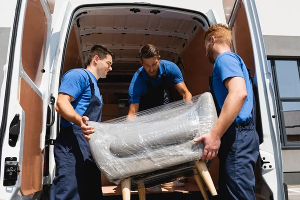 Loaders unloading armchair in stretch wrap from truck on urban street — Stock Photo