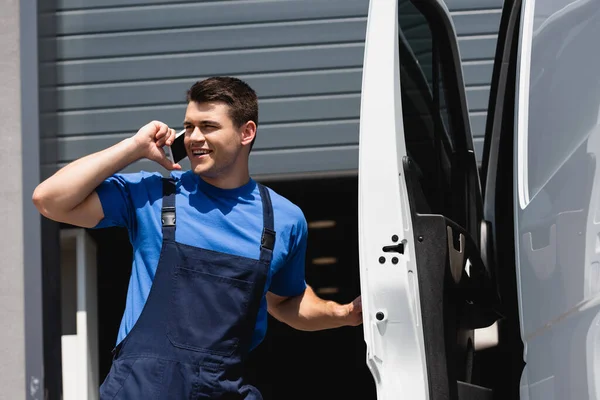 Завантажувач в уніформі, дивлячись подалі, розмовляючи по смартфону біля вантажівки на міській вулиці — стокове фото