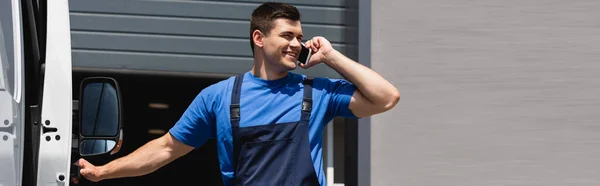 Horizontal crop of loader talking on smartphone near truck on urban street — Stock Photo