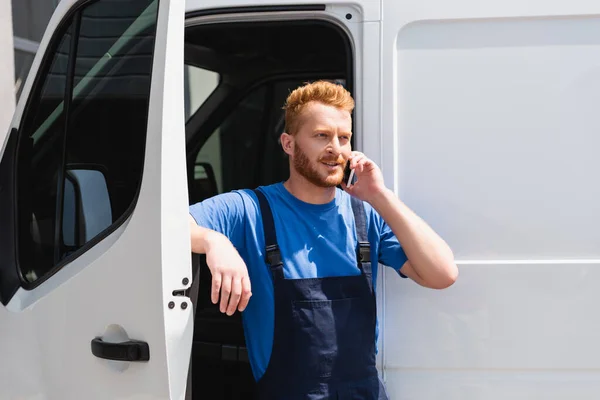 Jeune chargeur parlant sur téléphone portable tout en se tenant près du camion à l'extérieur — Photo de stock
