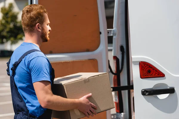 Side view of loader holding package near truck on urban street — Stock Photo