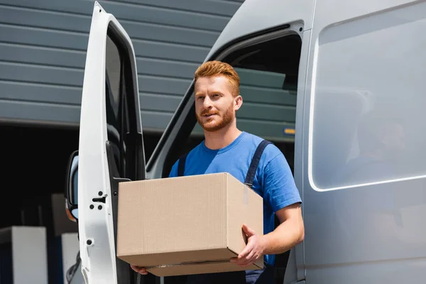 Loader in uniform carrying cardboard box near truck on urban street — Stock Photo