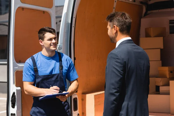 Loader with pen and clipboard looking at businessman near truck on urban street — Stock Photo