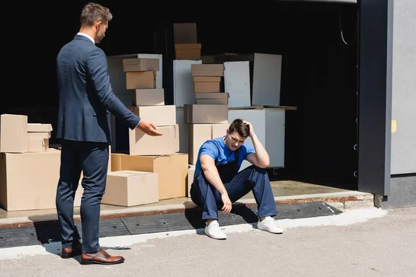 Homme d'affaires pointant avec la main près de chargeur bouleversé dans l'entrepôt à l'extérieur — Photo de stock