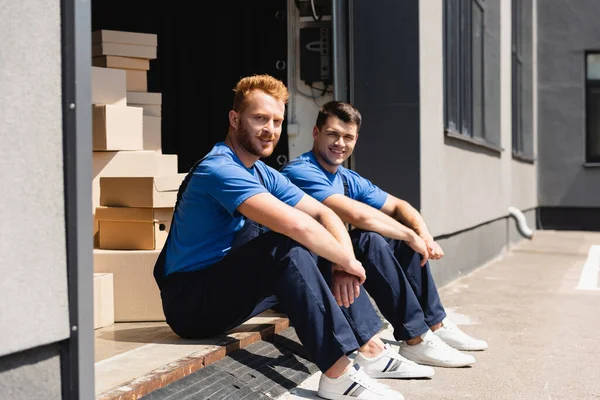 Selective focus of loaders looking at camera while sitting in warehouse outdoors — Stock Photo