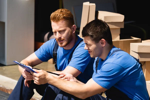 Loader pointing at clipboard beside colleague in warehouse outdoors — Stock Photo