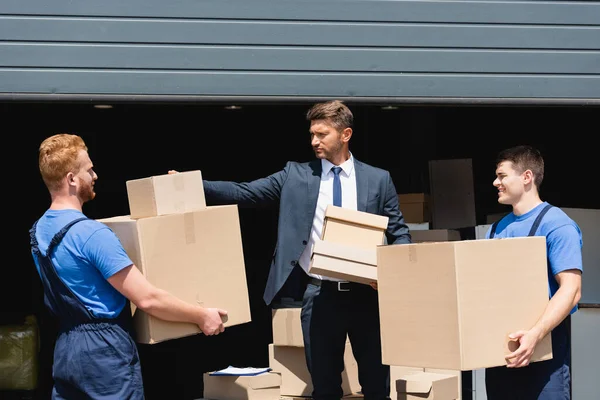 Businessman stacking cardboard boxes near loaders and warehouse outdoors — Stock Photo