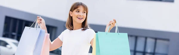 Panoramic crop of woman in white t-shirt holding shopping bags on urban street — Stock Photo