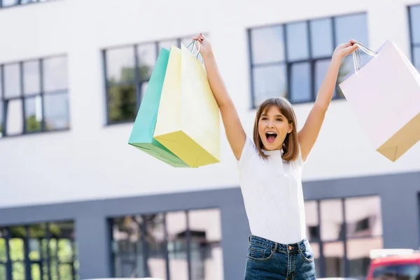 Excited woman in white t-shirt holding colorful shopping bags on urban street — Stock Photo