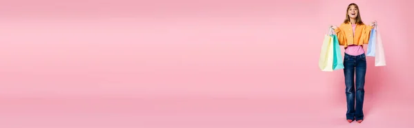 Панорамна концепція молодої жінки, що тримає барвисті сумки для покупок на рожевому фоні — стокове фото
