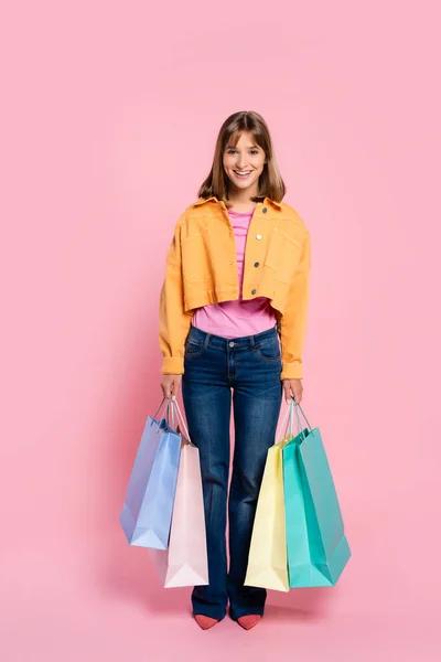 Mujer joven mirando a la cámara mientras sostiene bolsas de compras de colores sobre fondo rosa — Stock Photo