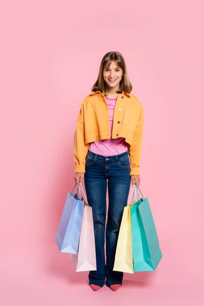 Jeune femme regardant la caméra tout en tenant des sacs à provisions colorés sur fond rose — Photo de stock