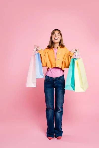 Excited woman in yellow jacket holding purchases and looking at camera on pink background — Stock Photo