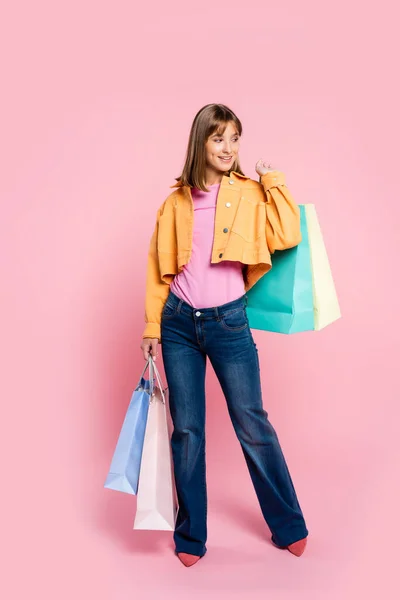 Mulher olhando para longe enquanto segurando sacos de compras coloridos no fundo rosa — Fotografia de Stock