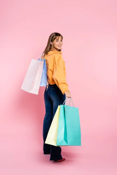 Mujer con chaqueta amarilla mirando a la cámara mientras sostiene bolsas de compras sobre fondo rosa — Stock Photo