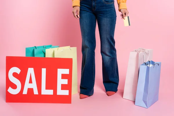 Vista recortada do cartão com letras de venda perto de sacos de compras e mulher segurando cartão de crédito no fundo rosa — Fotografia de Stock