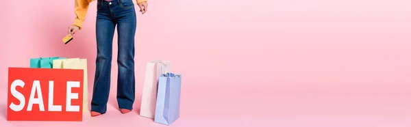 Panoramafahrt einer Frau mit Kreditkarte in der Nähe einer Karte mit Verkaufsaufdruck und Einkäufen auf rosa Hintergrund — Stockfoto