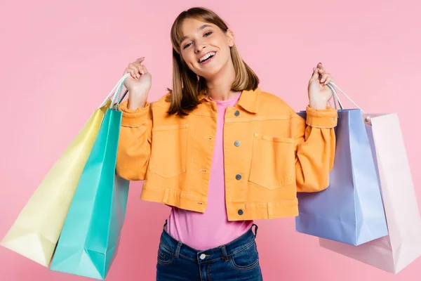 Young woman in yellow jacket holding colorful purchases on pink background — Stock Photo