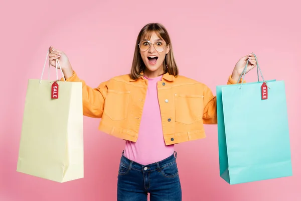 Femme surprise tenant des sacs à provisions avec lettrage de vente sur des étiquettes de prix sur fond rose — Photo de stock