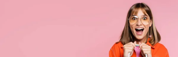 Панорамний знімок збудженої жінки в сонцезахисних окулярах дивиться на камеру ізольовано на рожевому — стокове фото