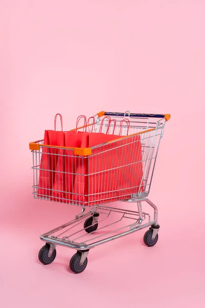 Sacos de compras vermelhos no carrinho na superfície rosa — Fotografia de Stock