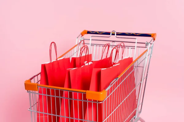 Sacos de compras vermelhos no carrinho no fundo rosa — Fotografia de Stock