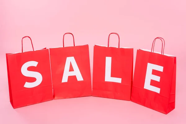 Red shopping bags with sale lettering on pink surface — Stock Photo