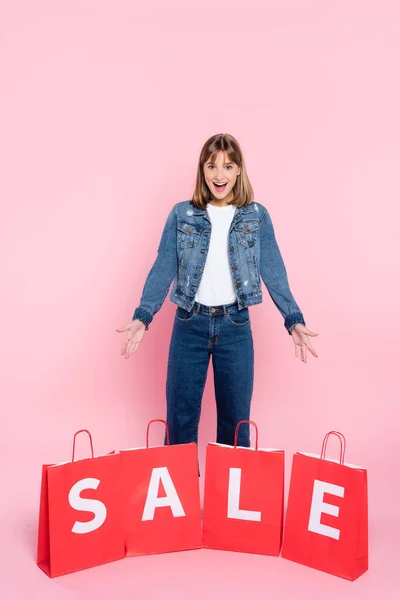 Giovane donna che punta con le mani a borse della spesa con la vendita lettering su sfondo rosa — Foto stock