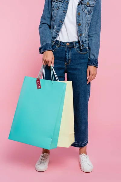 Cropped view of woman holding shopping bags with price tag and sale lettering on pink background — Stock Photo