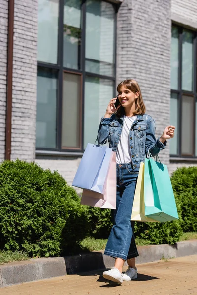 Mujer joven hablando en el teléfono inteligente mientras camina con bolsas de compras en la calle urbana - foto de stock