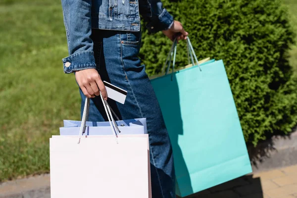 Vista cortada da jovem segurando cartão de crédito e sacos de compras na rua urbana — Fotografia de Stock